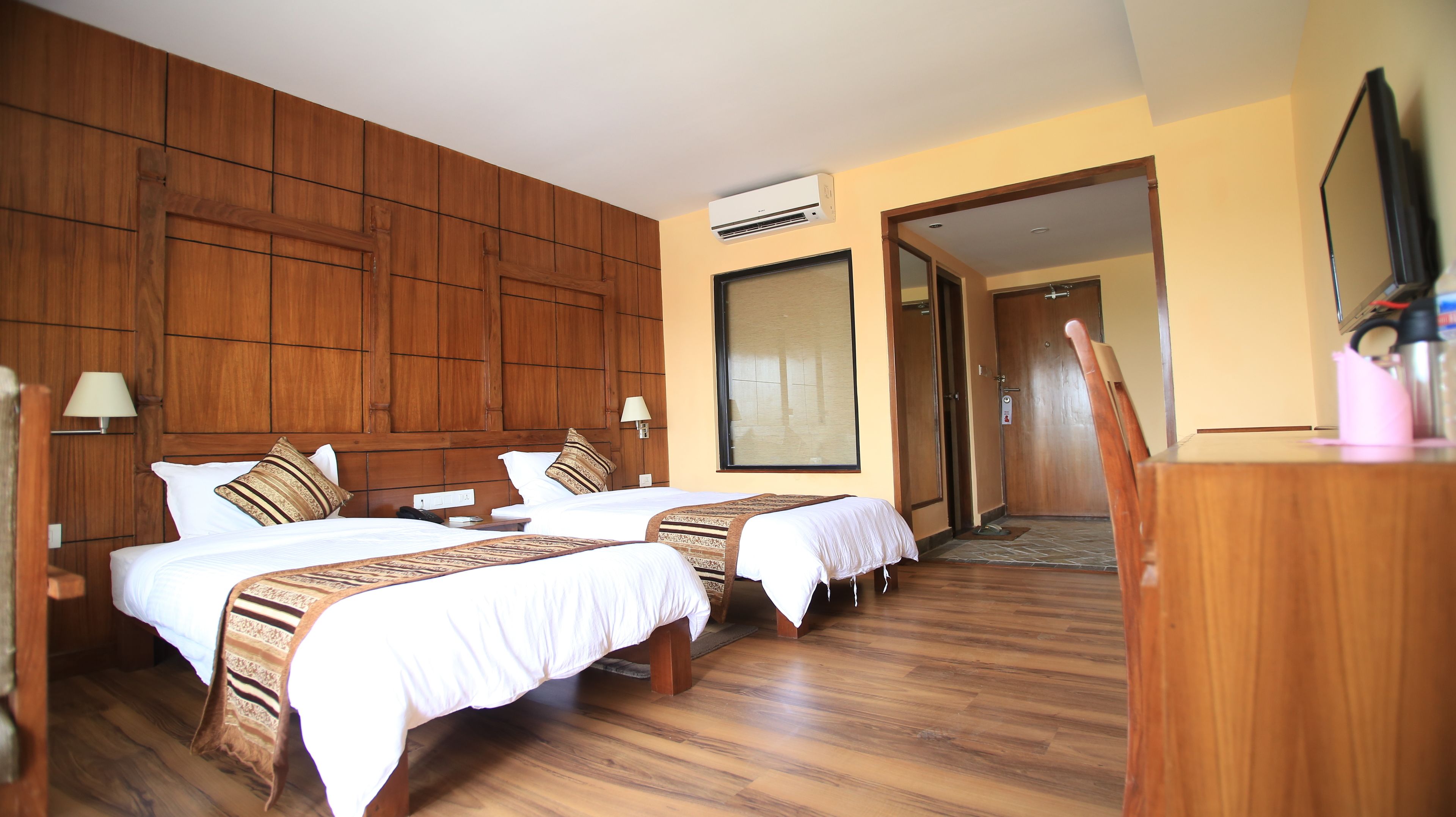 Una camera d'albergo con due letti, pannelli di legno sulle pareti, un'ampia finestra e un condizionatore d'aria.