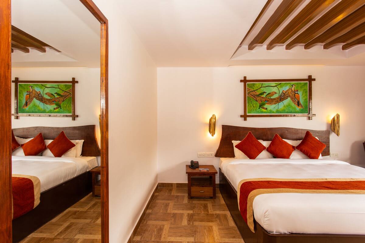 A hotel room with two beds, wooden headboards, a nightstand, a mirror, and two wall-mounted paintings.