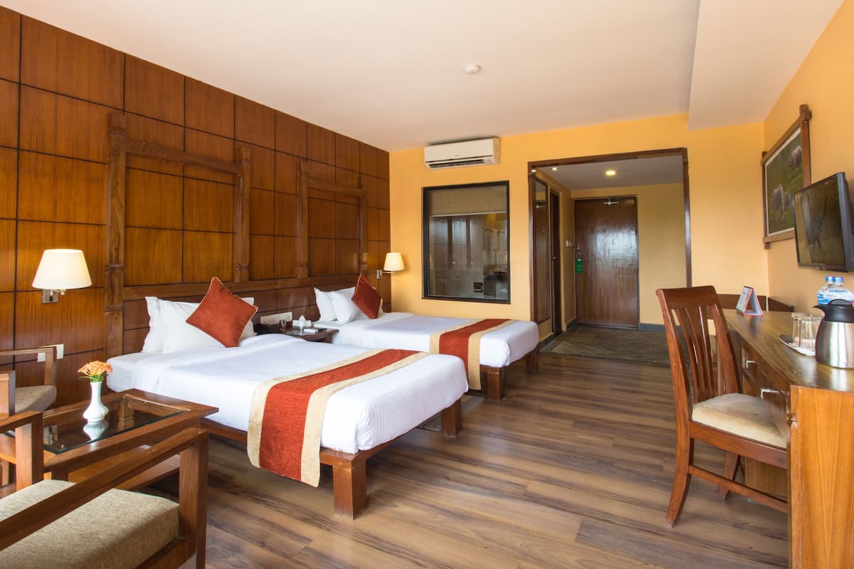 A hotel room with two beds, a desk, chairs, and a TV.