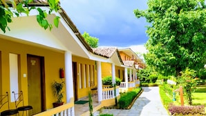 Una hilera de edificios amarillos con balcones blancos, un sendero de piedra y jardines verdes.