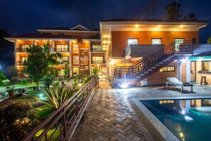 A hotel with a swimming pool, a well-lit garden, and a staircase leading to the upper floors. - Landmark Forest Park (Sauraha)