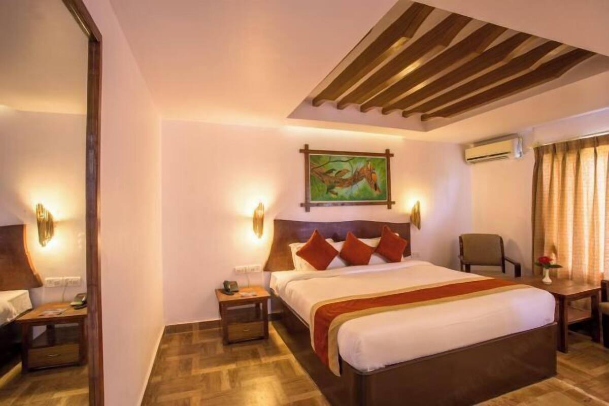 A hotel room with a bed, bedside tables, a chair, a desk, and a painting on the wall.