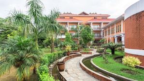 Un patio con un sendero curvo, palmeras y un edificio con tejados de tejas rojas.