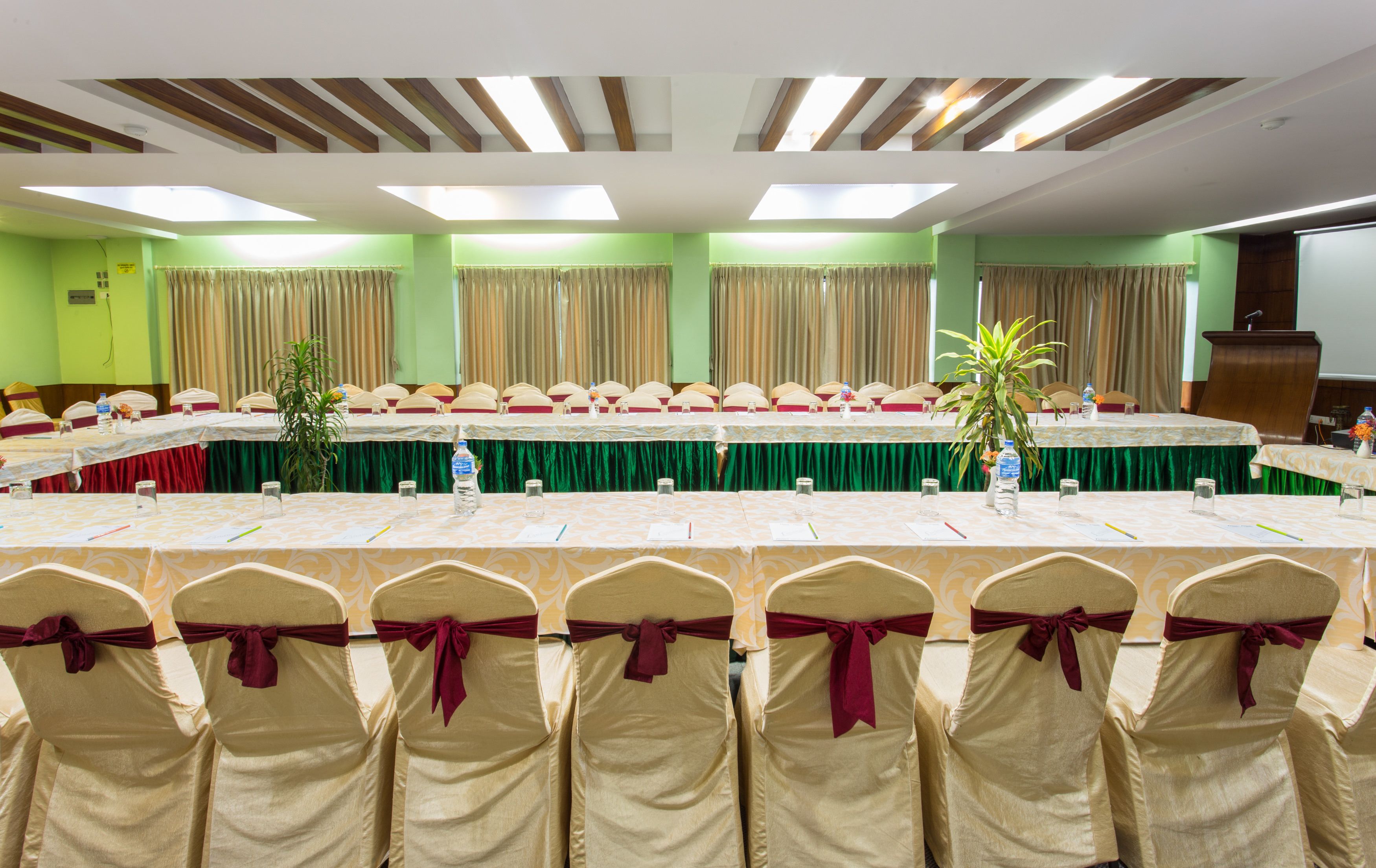 A conference room with a long table, chairs with red sashes, and green curtains.