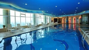 Ein Hallenbad mit klarem, blauen Wasser, Liegestühlen und großen Fenstern.