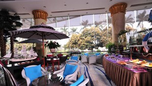 Ein geräumiger Innenbereich mit Rattanmöbeln, einem Buffet und großen Fenstern mit Blick auf Bäume und eine Palme.