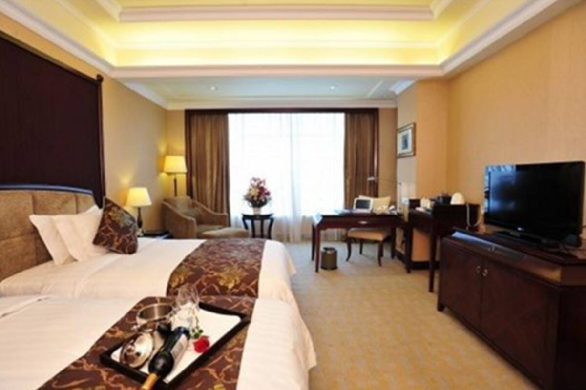 Ein Hotelzimmer mit zwei Betten, einem Schreibtisch, einem Fernseher und einem Esstisch mit Tablett.