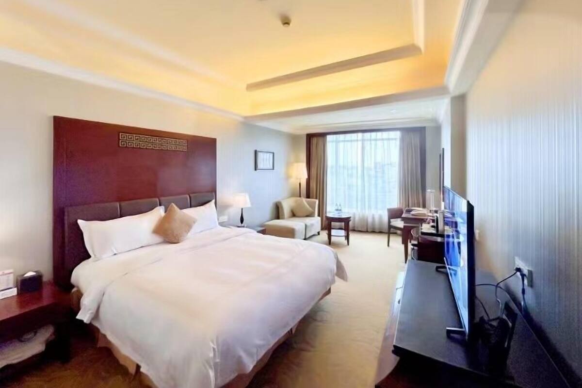 Ein Hotelzimmer mit einem großen Bett, einem Schreibtisch mit Computer, einem Stuhl und einem Fernseher.