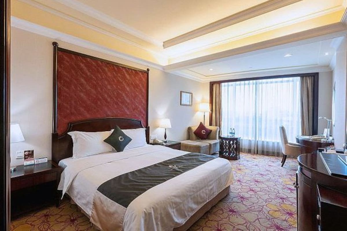 A hotel room with a large bed, a desk, a chair, and a window with curtains.