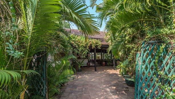 A stone pathway leading to a covered seating area surrounded by lush greenery and potted plants. - SiZen Retreat & Spa (Siem Reap)