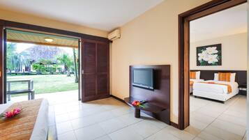 A hotel room with a bed, a TV, a small table with a flower, and a view of the garden and pool area.
