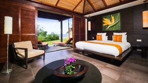 Ein modernes Schlafzimmer mit einem großen Bett, einem Sessel, einem Couchtisch mit Blumen und Blick ins Freie.