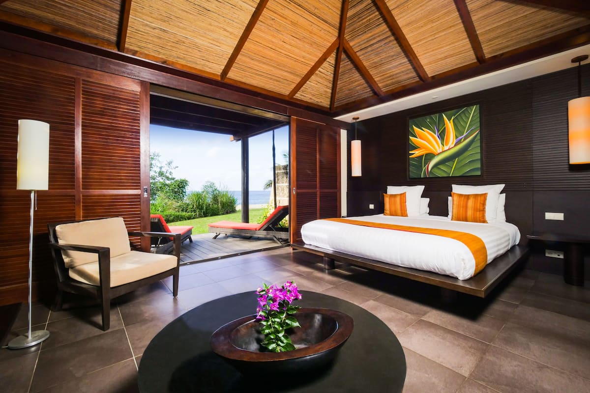Um quarto moderno com uma cama grande, uma cadeira, uma mesa de centro com flores e vista para o exterior.