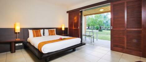 Une chambre d’hôtel avec un grand lit, deux lampes de chevet, une tête de lit en bois et une vue sur un jardin, accessible par une porte coulissante.