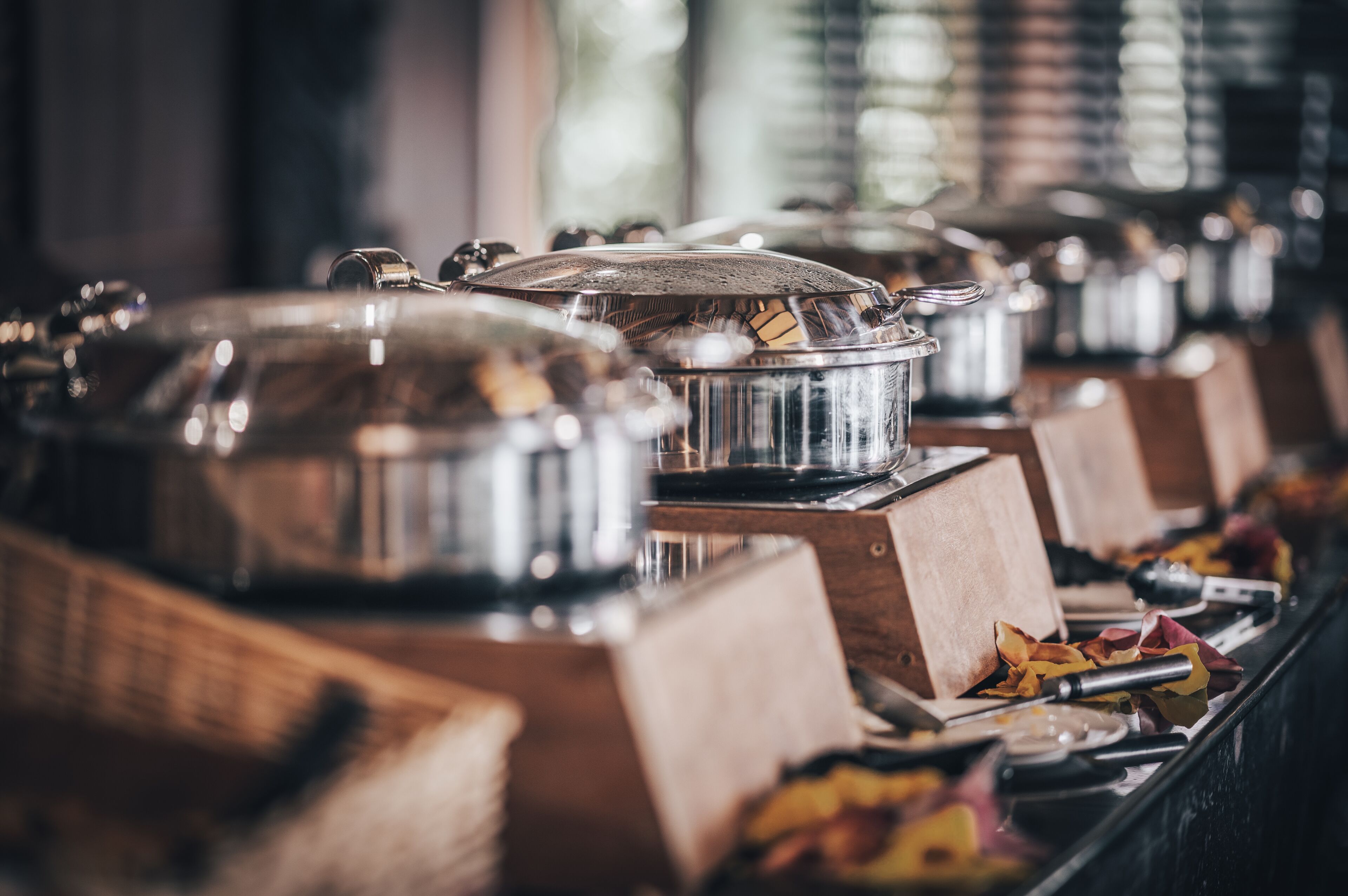 Una barra de buffet con recipientes para alimentos cubiertos sobre puestos de madera.
