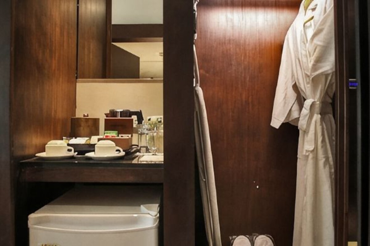 Habitación de hotel con puerta de madera, una bata blanca colgada en la puerta y un mostrador con tazas y una tetera.