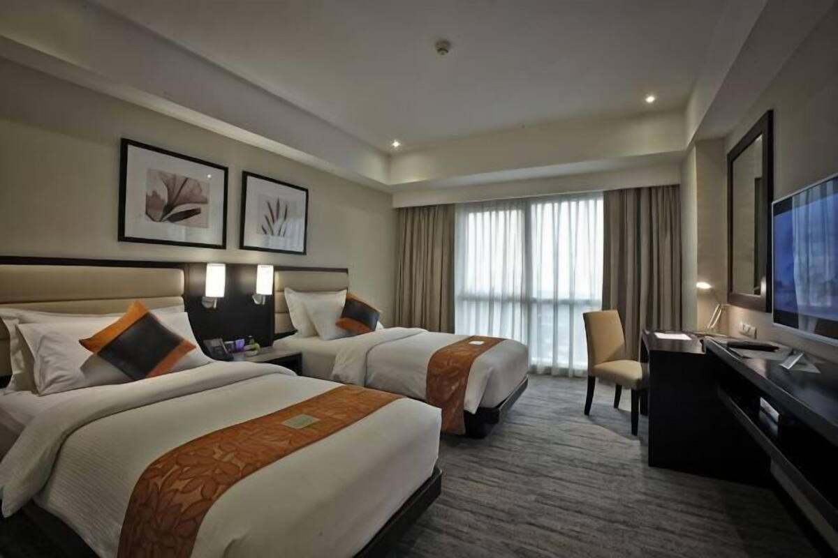 Habitación de hotel con dos camas, un escritorio, una silla, un televisor y cuadros en la pared.