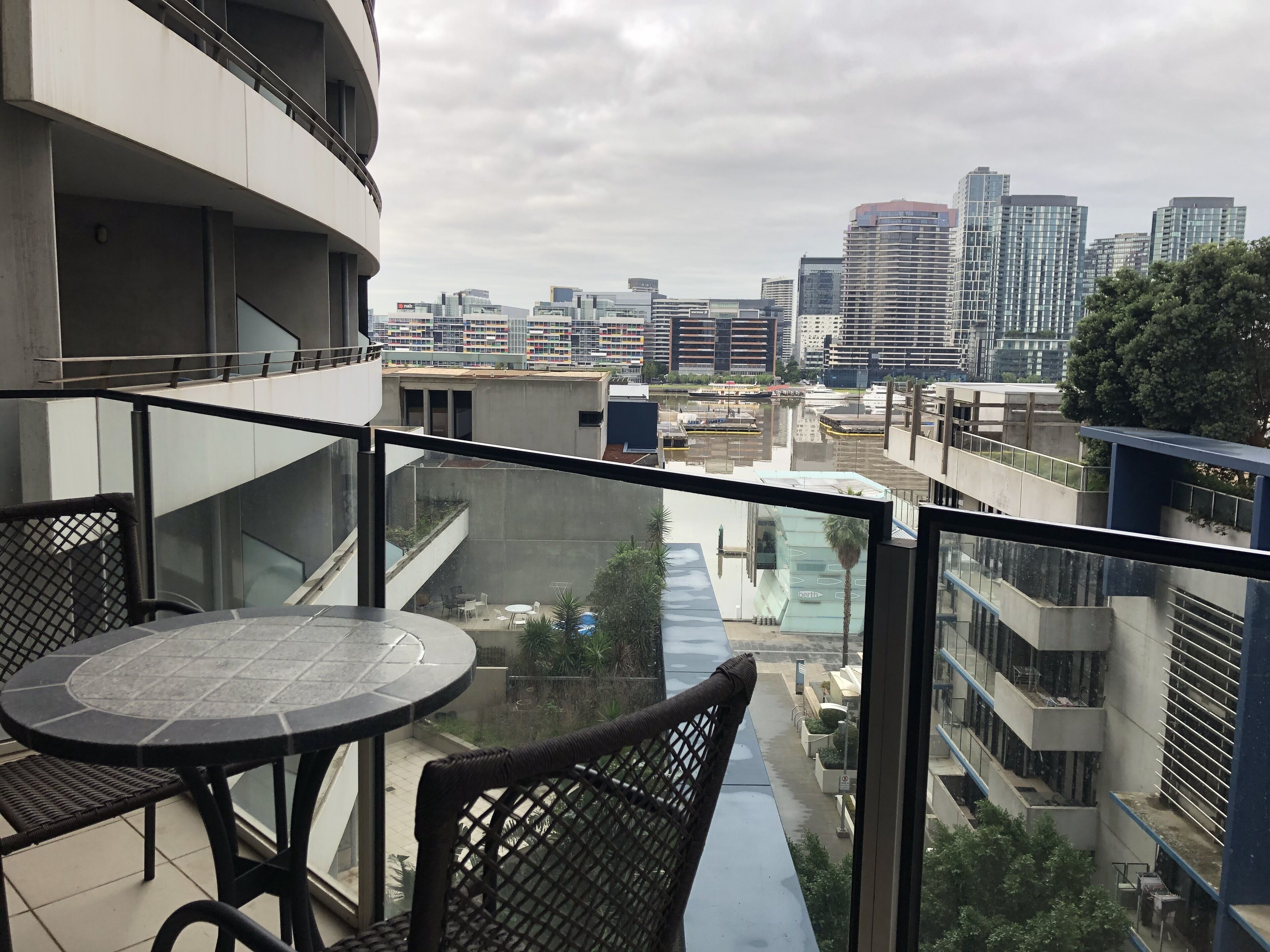 A balcony with a round table and chairs, overlooking a cityscape with modern buildings and a river.