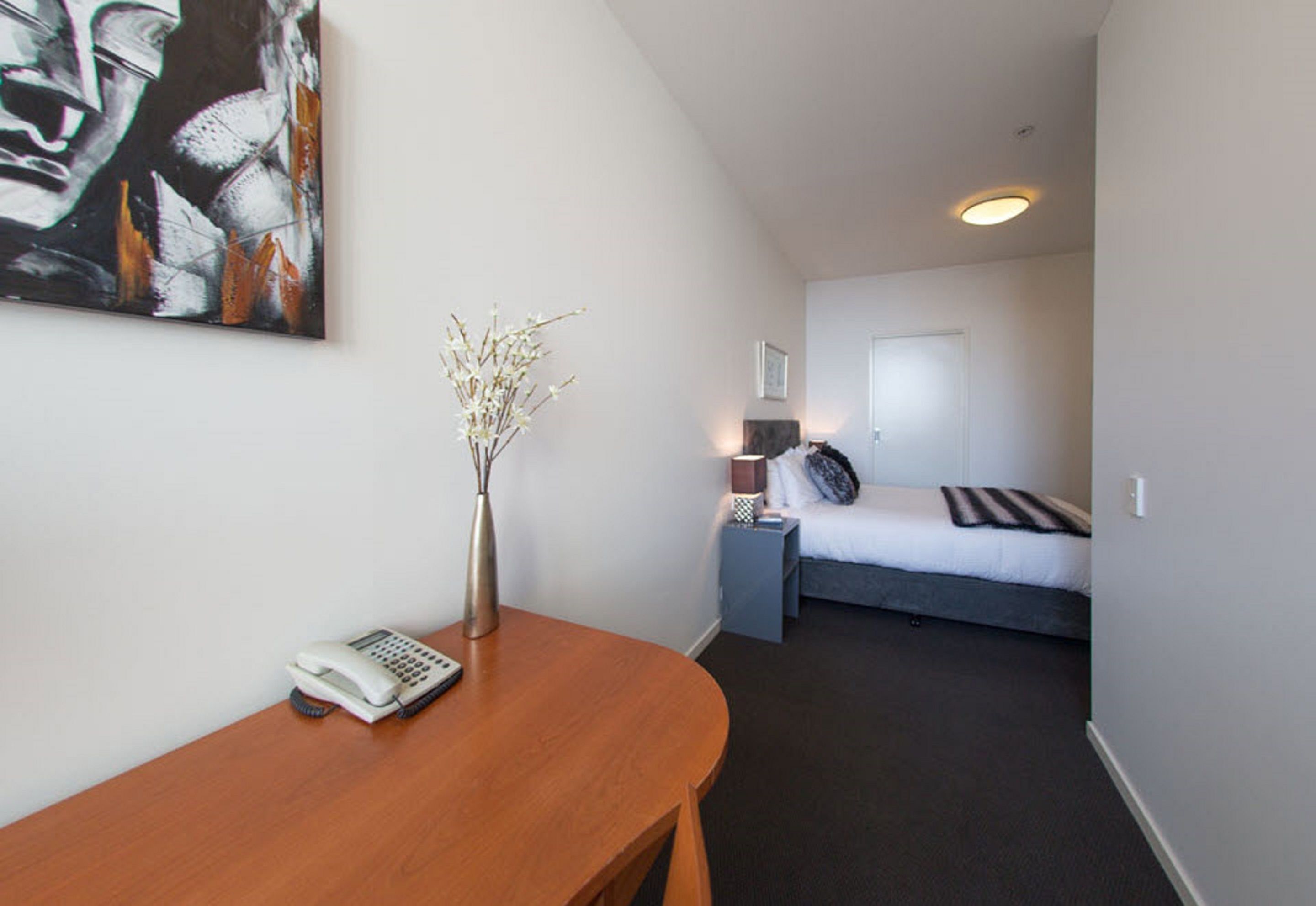 A hotel room with a bed, bedside table, lamp, and a painting on the wall.
