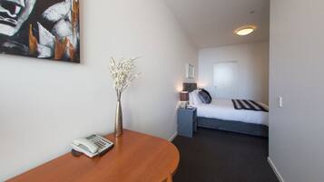A hotel room with a bed, bedside table, lamp, and a painting on the wall.