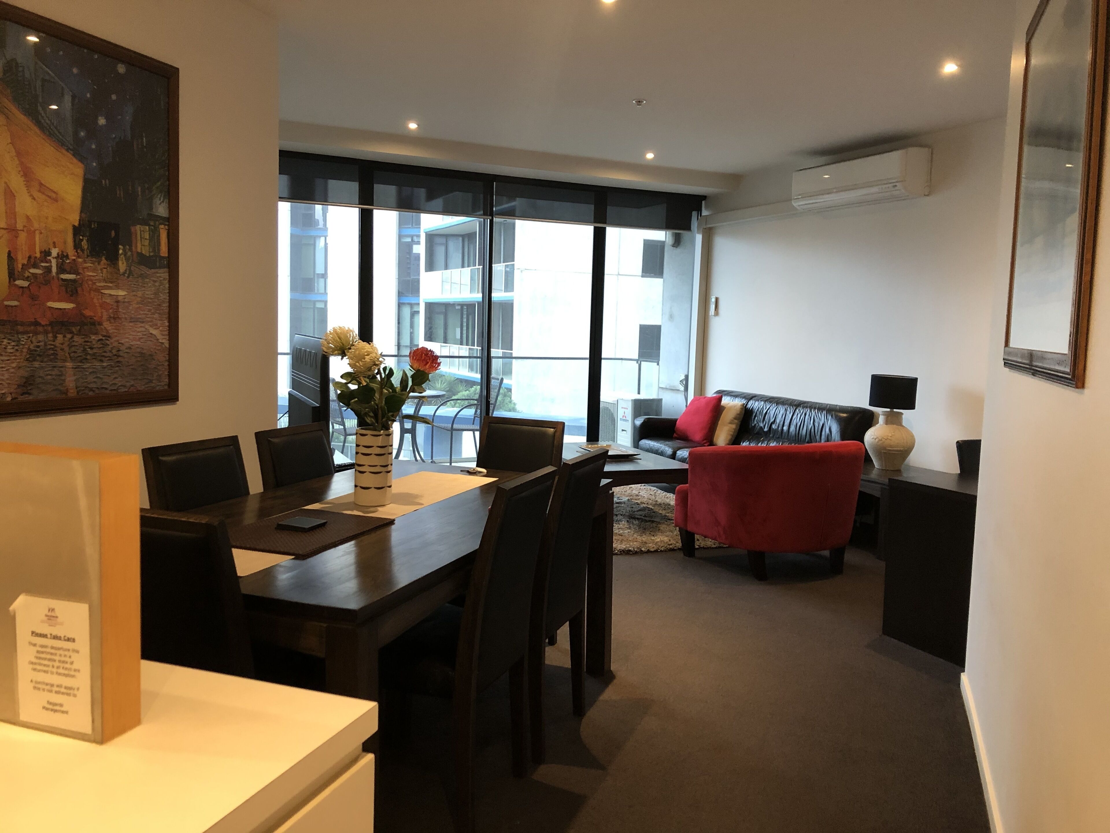 A modern hotel room with a dining area, a sofa, and a large window offering a city view.