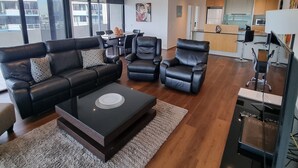 A modern living room with a black leather sofa, a coffee table, and a dining area with a table and chairs.