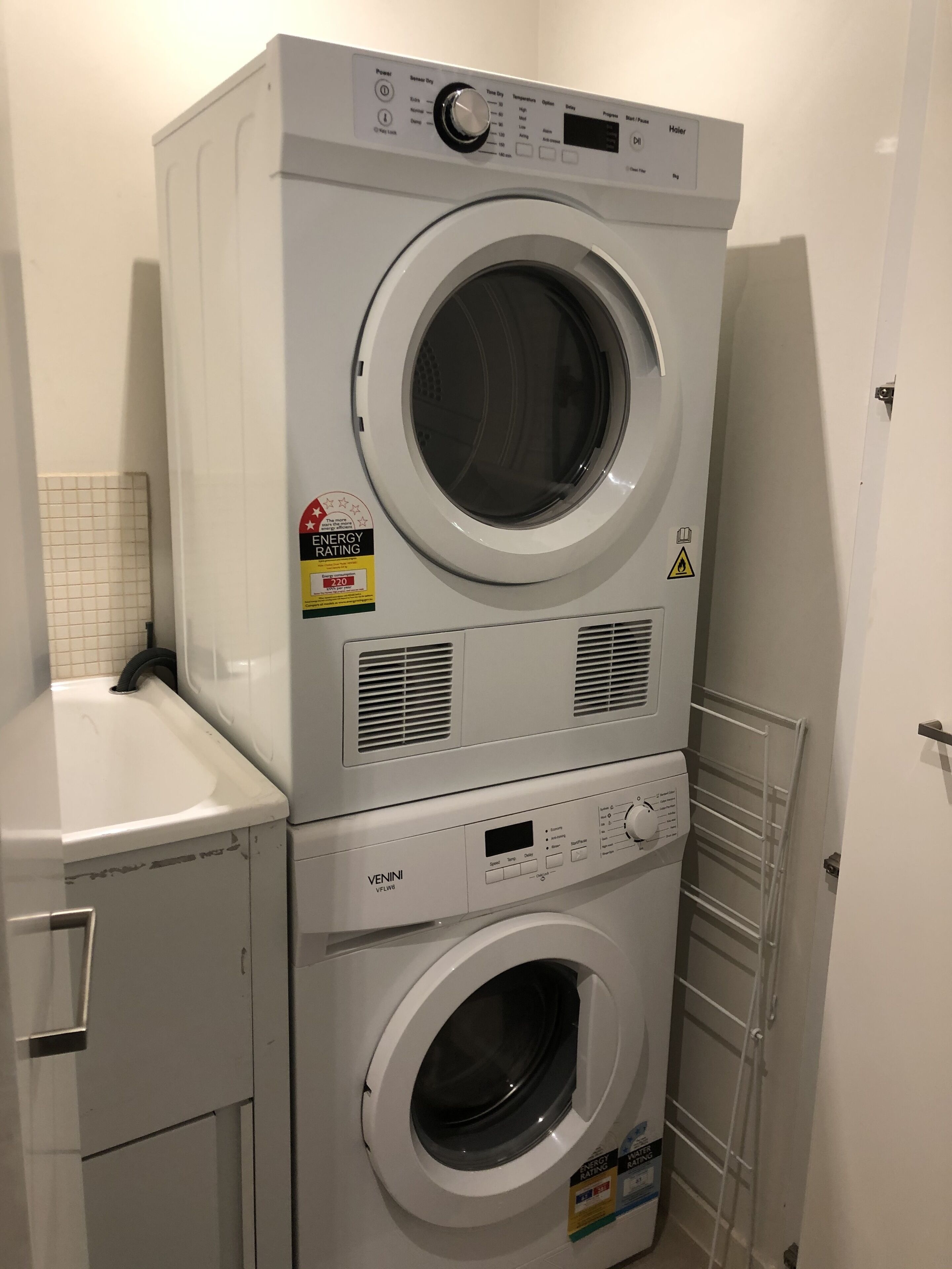 A stacked washer and dryer unit in a laundry room with a tiled wall and a door.