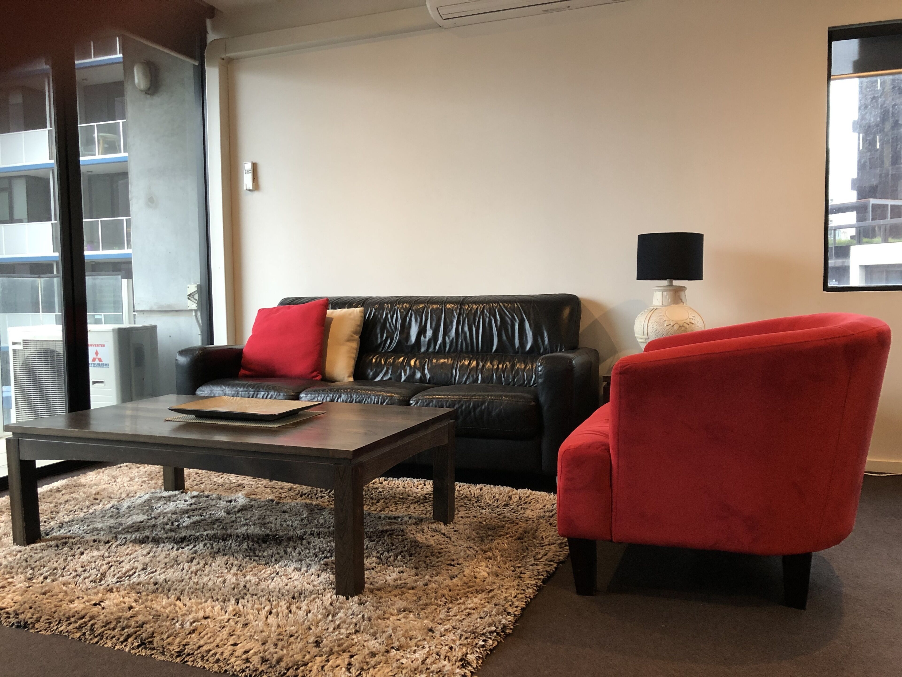 A living room with a black leather sofa, a red armchair, a coffee table, and a lamp.