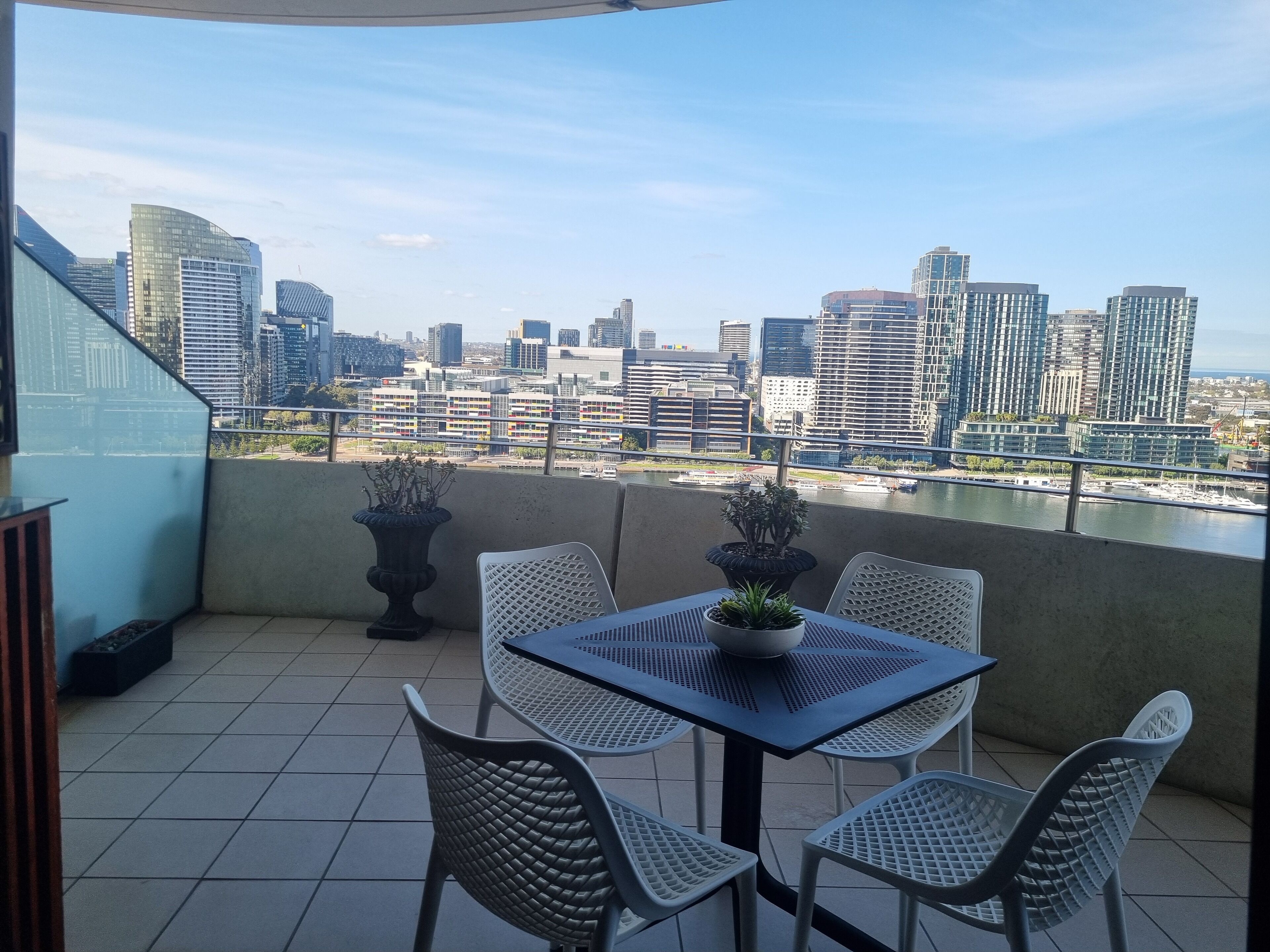 A balcony with a table and chairs, potted plants, and a city view.