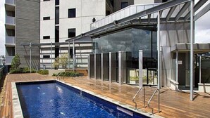 A modern outdoor swimming pool with a wooden deck, surrounded by a glass-enclosed structure.