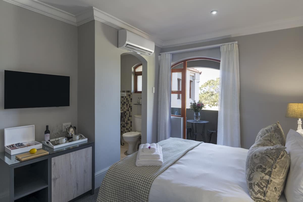 A hotel room with a bed, a TV mounted on the wall, a small table with a tray of breakfast items, and an air conditioning unit.