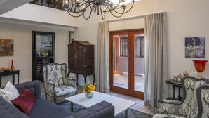 A spacious living room with a chandelier, a sofa, a coffee table with flowers, and a view to the outside. - Villa Tuscana By Mantis (Gqeberha (Port Elizabeth))