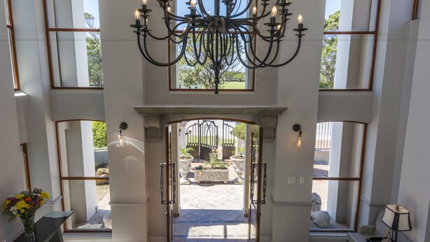 A grand entrance with a chandelier, a view of the courtyard, and a bench with a statue. - Villa Tuscana By Mantis (Gqeberha (Port Elizabeth))