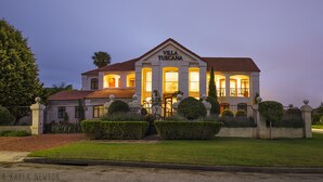 A large, elegant villa with a classic Tuscan architectural style, featuring a prominent entrance with a sign, well-maintained gardens, and a well-lit facade. - Villa Tuscana By Mantis (Gqeberha (Port Elizabeth))
