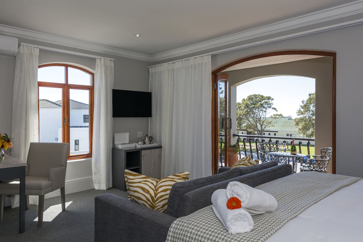 A hotel room with a bed, a desk, a chair, a TV, and a balcony with outdoor furniture.