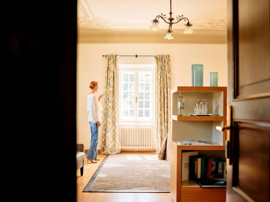 Une pièce avec une grande fenêtre, un radiateur, une bibliothèque en bois et une personne debout près de la fenêtre.