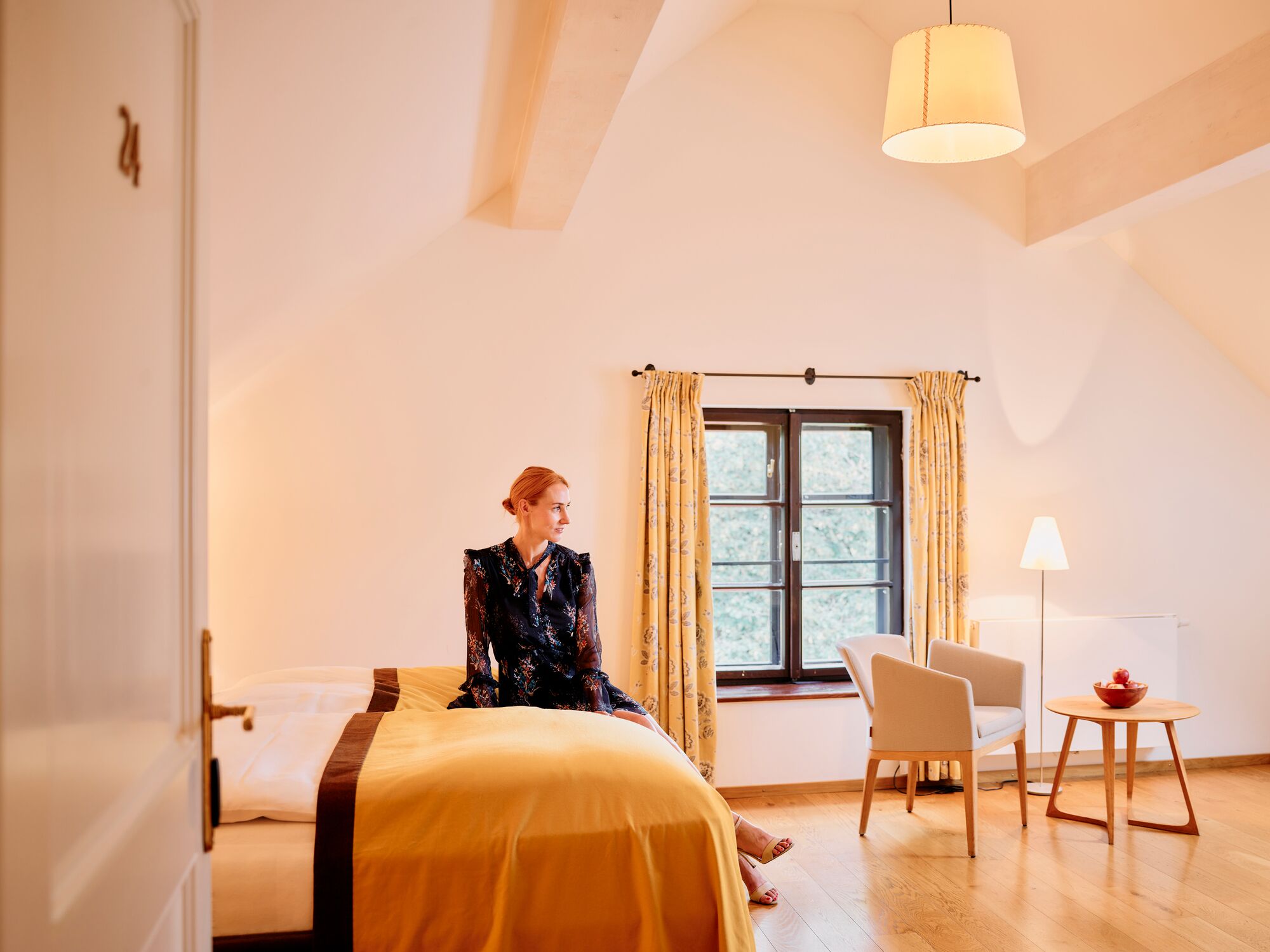 Una habitación con cama, una silla, una mesa y un ventanal con cortinas.