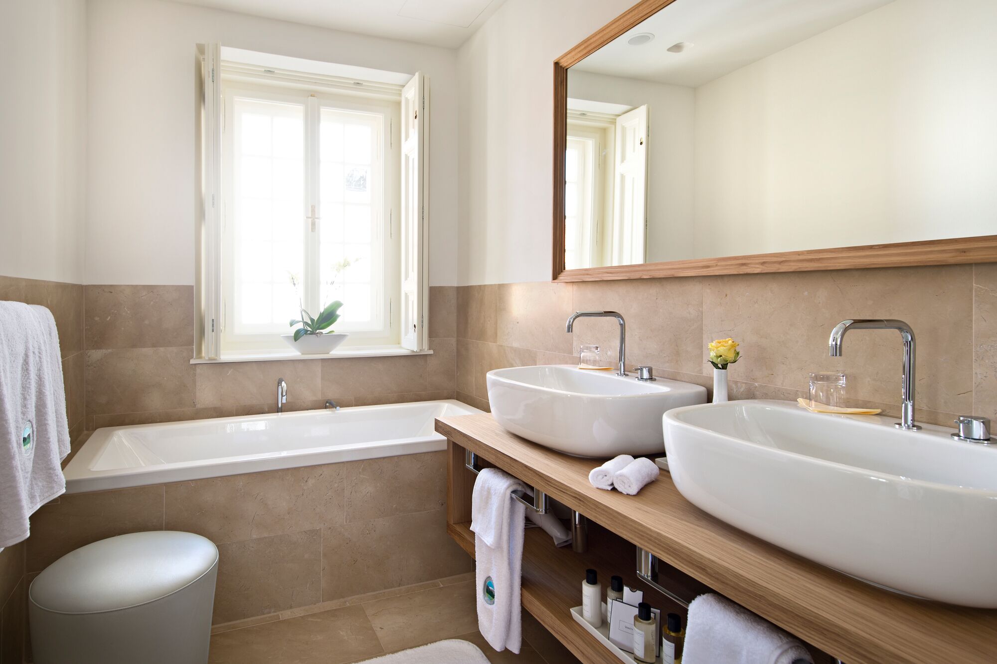 A modern bathroom with two sinks, a bathtub, a window with a plant, and a large mirror.
