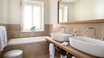 A modern bathroom with two sinks, a bathtub, a window with a plant, and a large mirror.