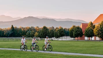 Tres ciclistas en un sendero pavimentado en una zona con césped, con un edificio de ladrillo y árboles al fondo.