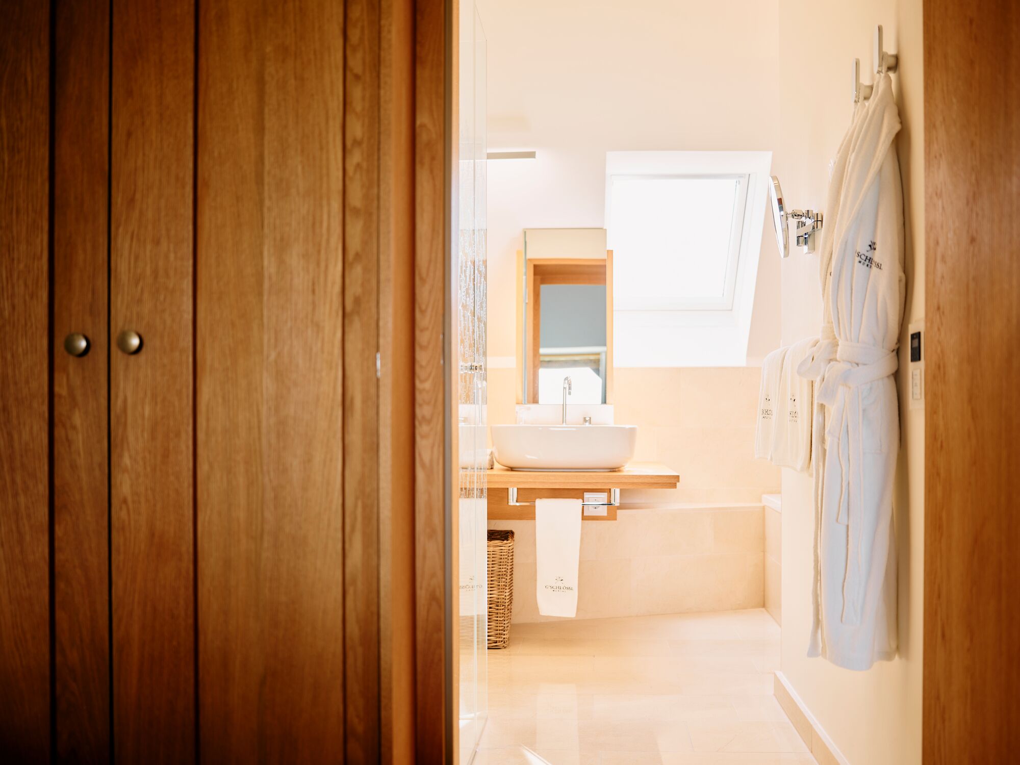 A wooden door leading to a bathroom with a sink, mirror, and hanging robes.