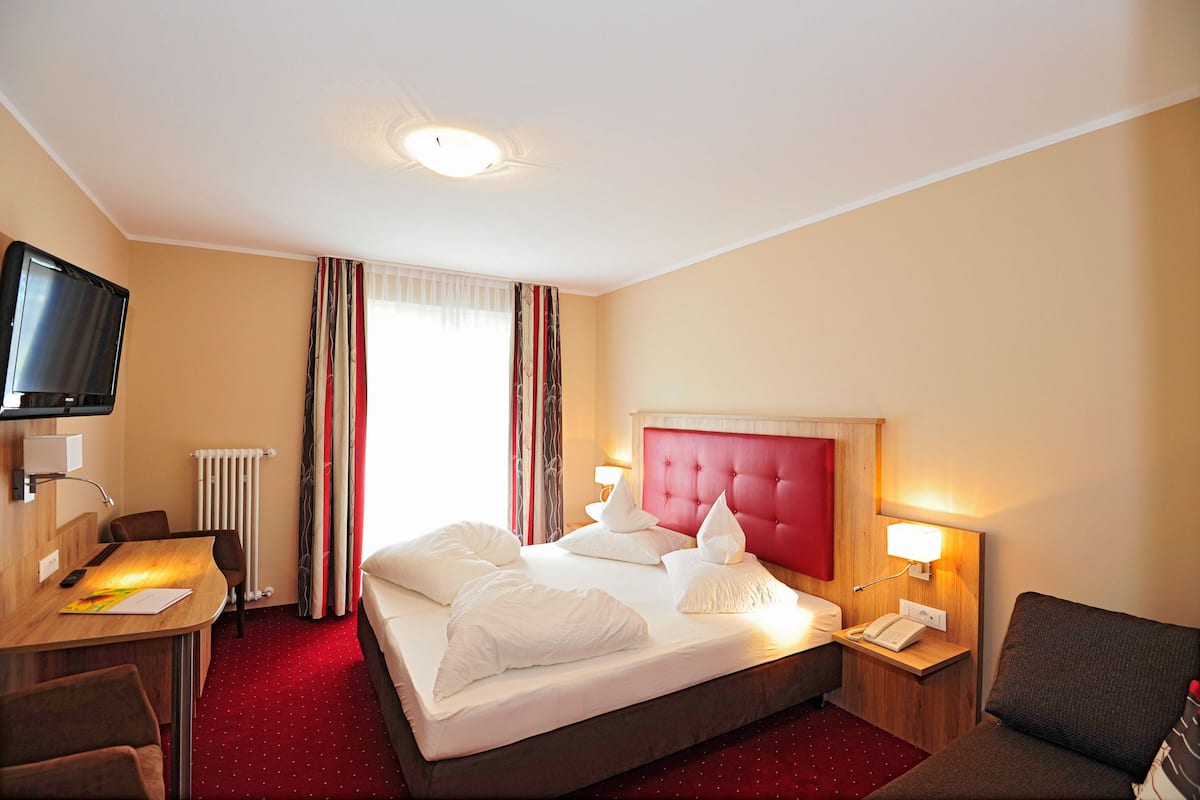 A hotel room with a bed, a desk, a chair, a TV, and a window with curtains.