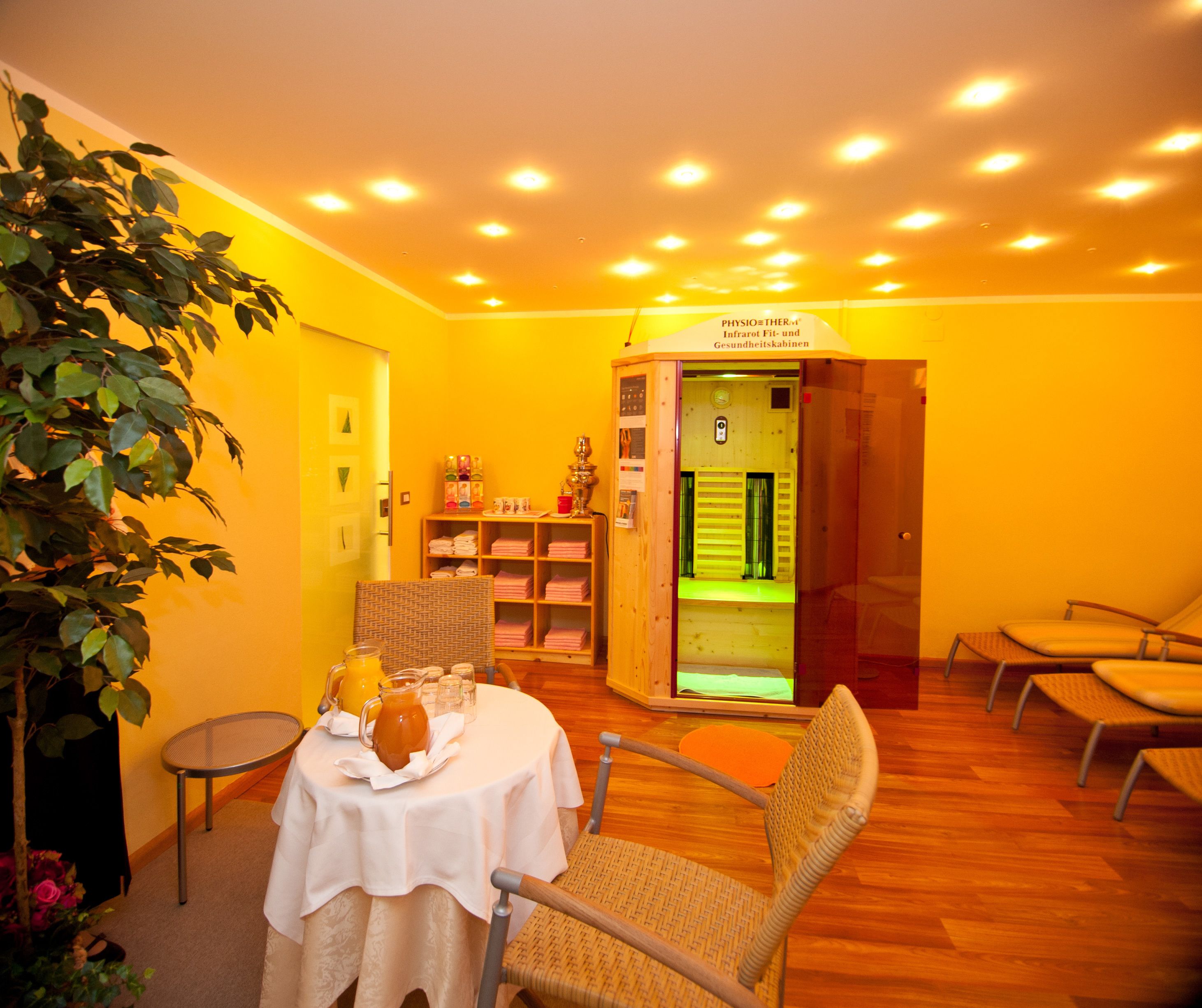 A room with a table set for two, a chair, a bookshelf, and a cabinet with a green-lit interior.