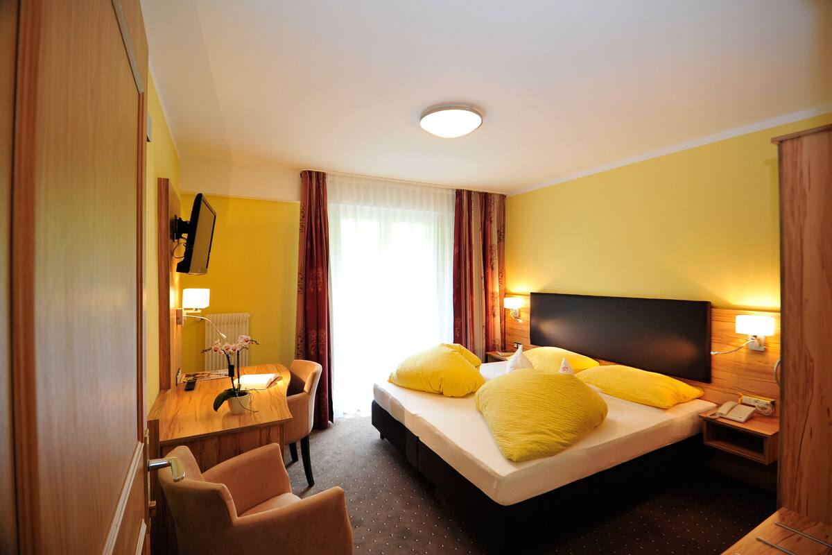 A hotel room with a bed, a desk, a chair, a TV, and a window with curtains.