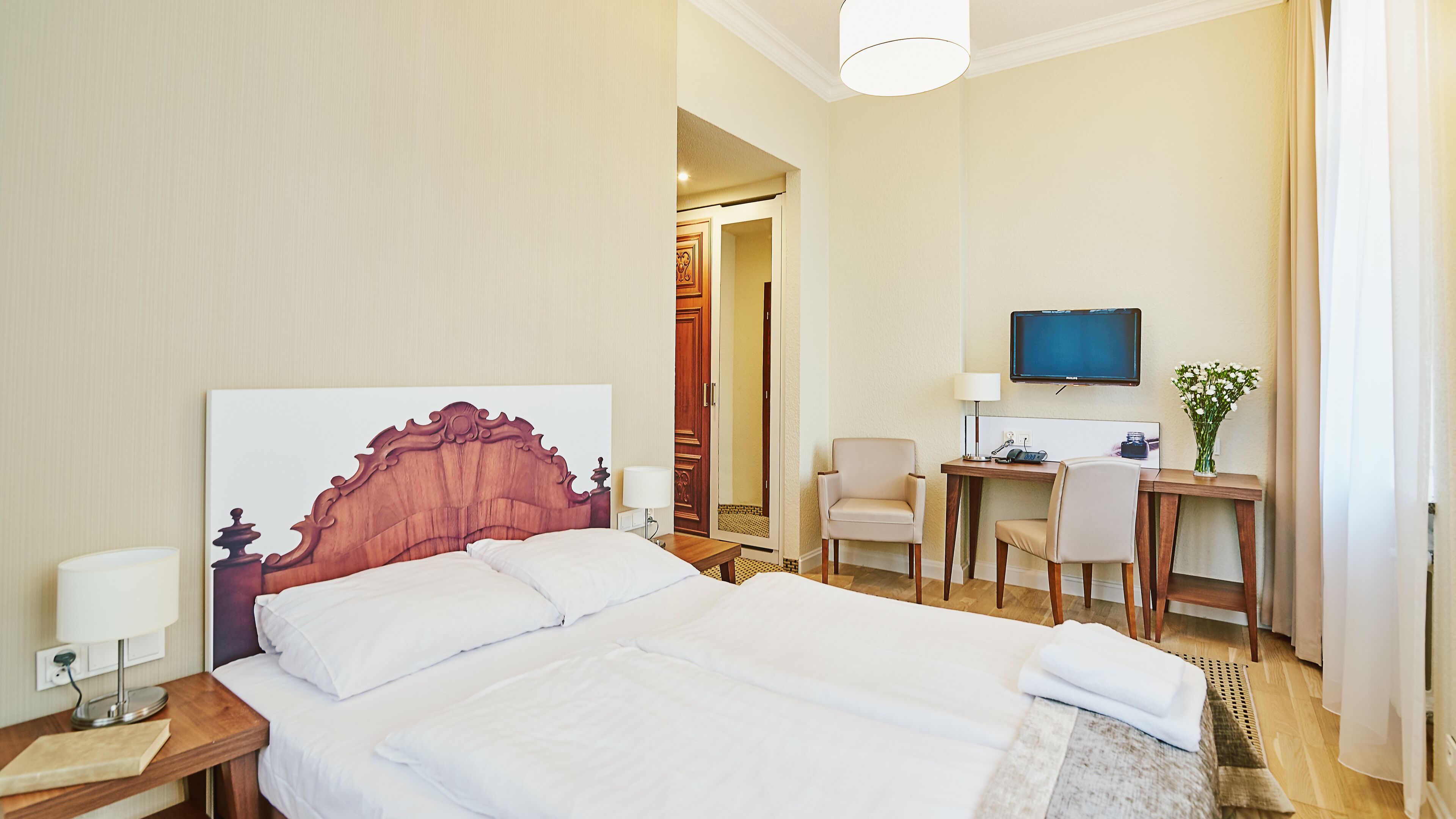 A hotel room with a large bed, a desk with a chair, a television, and a door leading to another room.