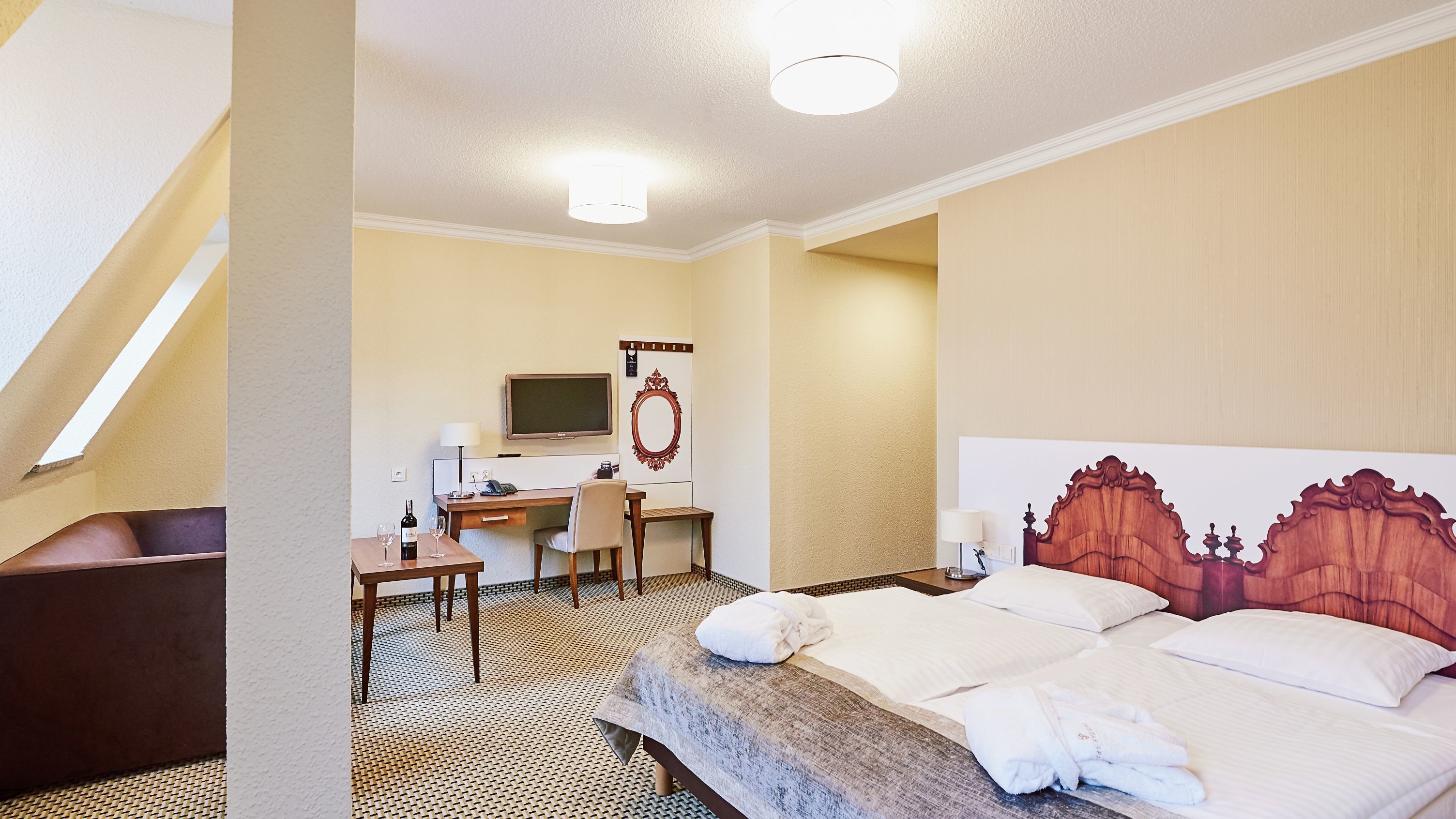 Una habitación de hotel con cama, escritorio, silla, televisor y espejo.