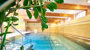 Una piscina interior con agua cristalina, rodeada de paredes de madera y una barrera de vidrio.