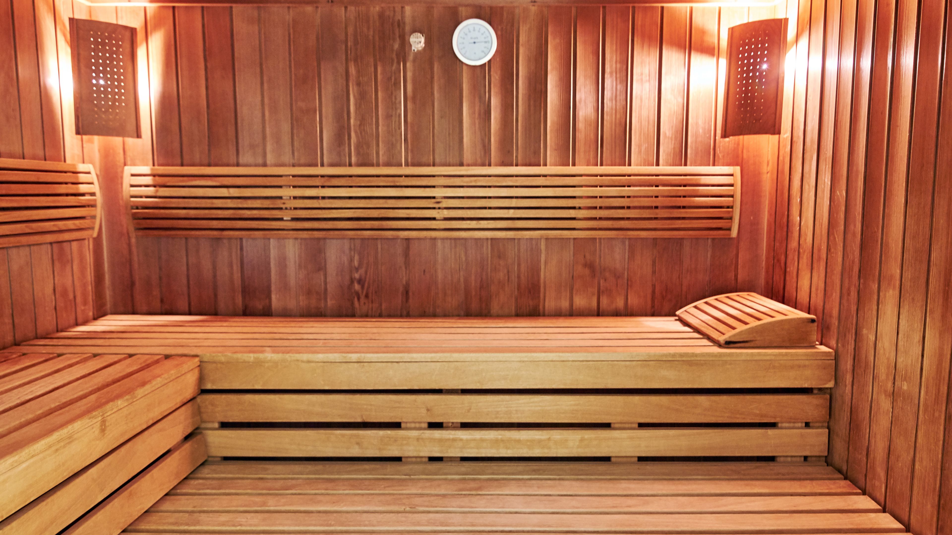 Un sauna avec des bancs et des murs en bois, un thermomètre bien visible et des panneaux de ventilation.