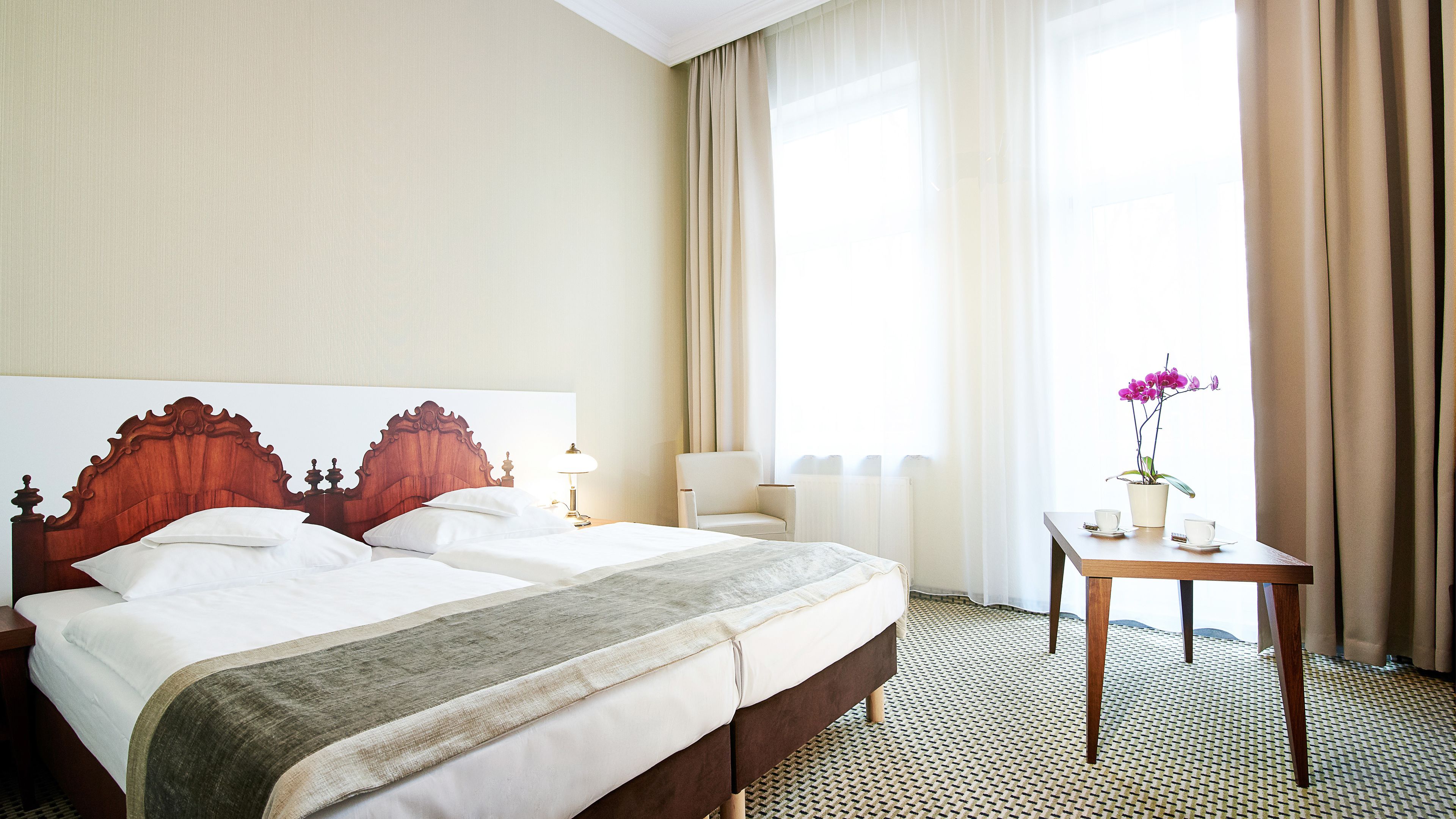 Ein Hotelzimmer mit einem großen Bett, einem Nachttisch mit Lampe, einem Sessel und einem Fenster mit Vorhängen.