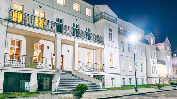 Un hotel de varios pisos con una entrada imponente, una escalera que conduce a la entrada principal y un jardín bien cuidado.